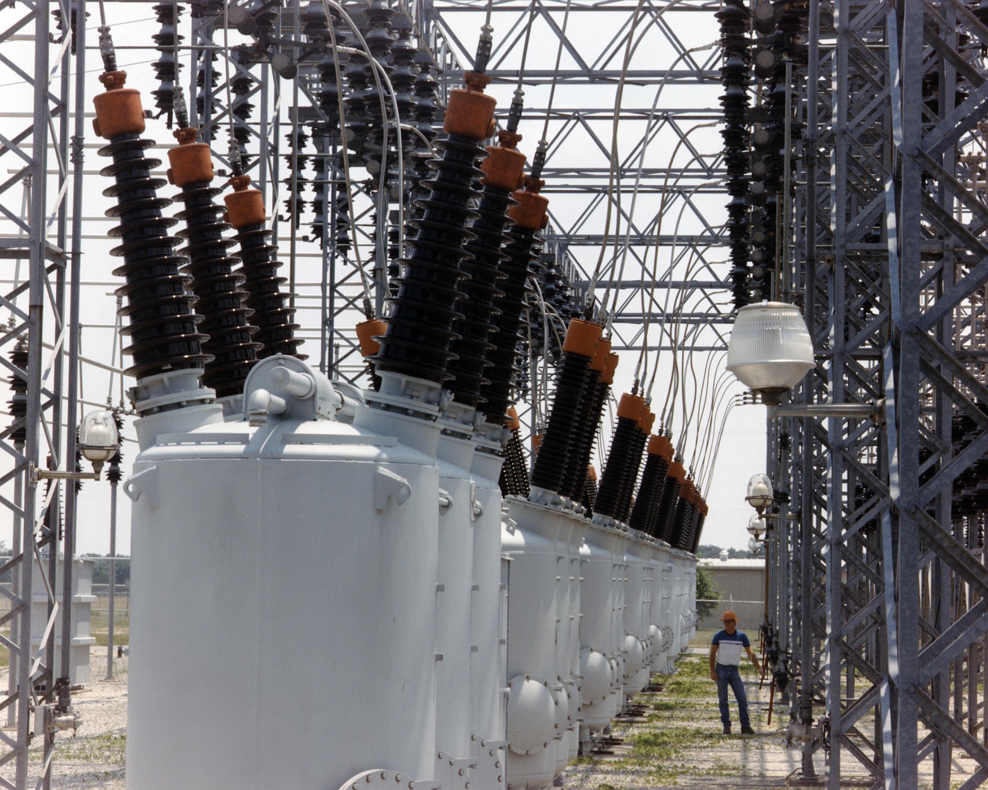 A worker stands among large electrical equipment and steel structures at an Oklahoma electricity switchyard.