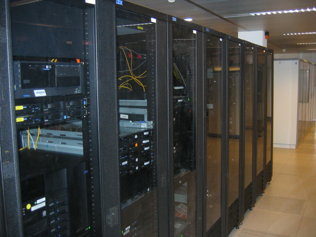 A row of black server cabinets with computer equipment and yellow cables in a data center.