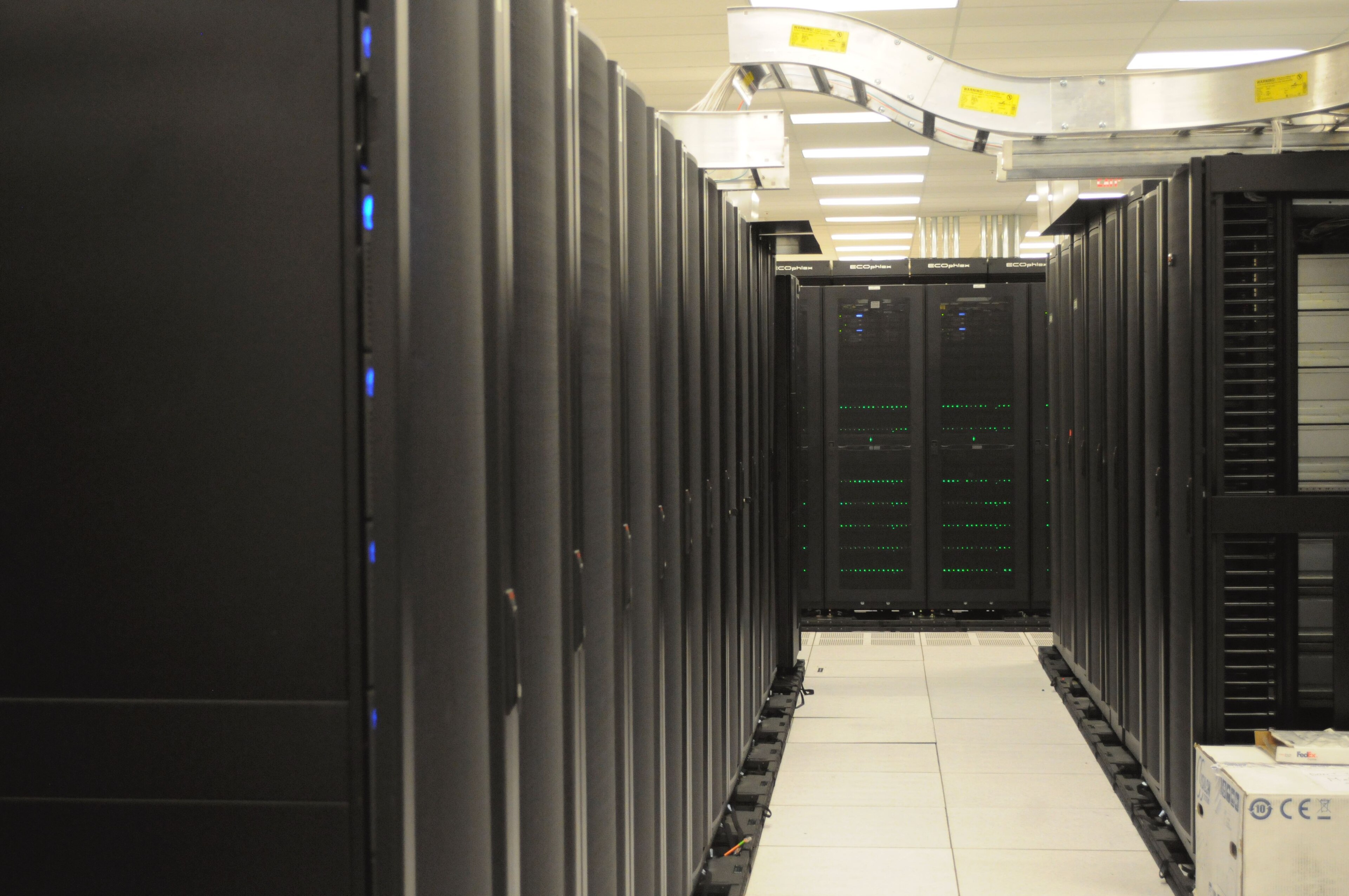 An aisle between black server racks with overhead cable trays at NERSC in an archival 2011 photograph.