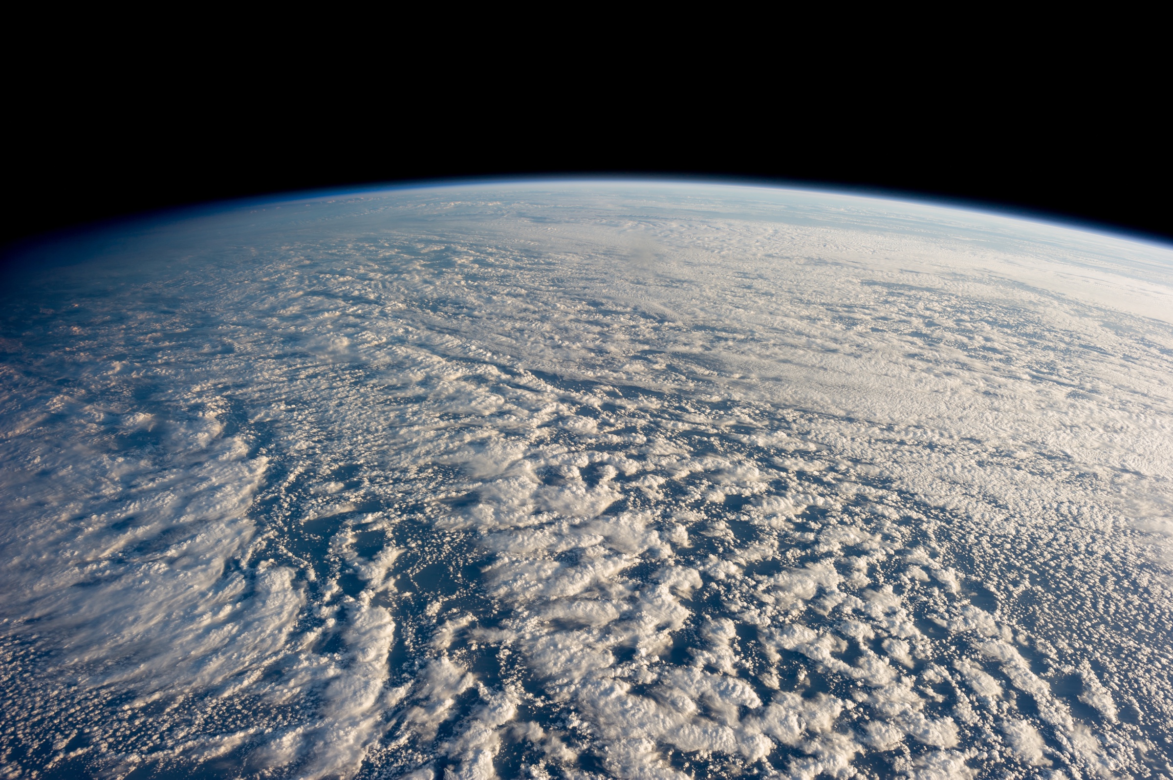 Low clouds cover the Pacific Ocean beneath the curved horizon of Earth, seen from orbit.