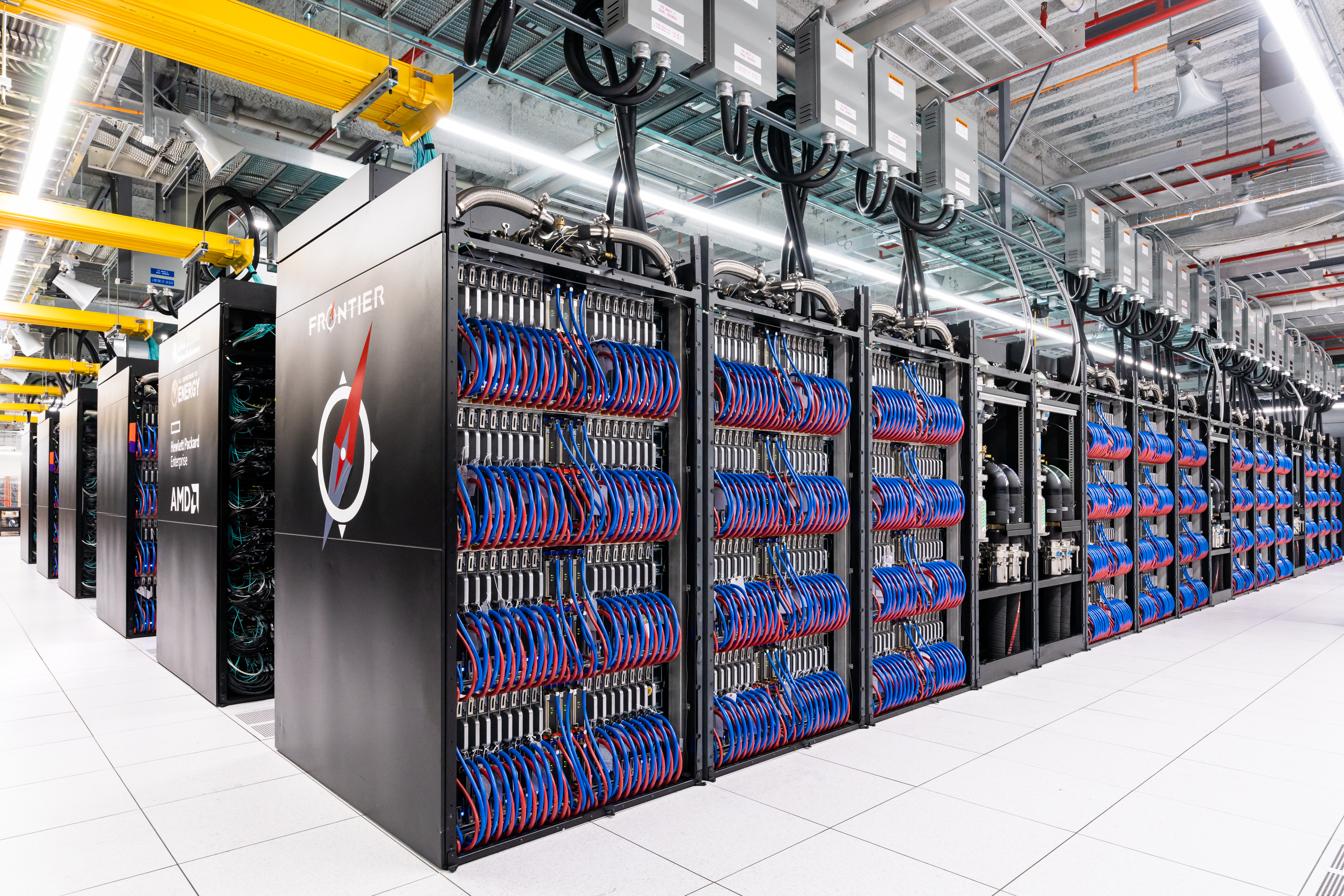Rows of open black Frontier supercomputer cabinets with blue and red cabling at Oak Ridge National Laboratory.