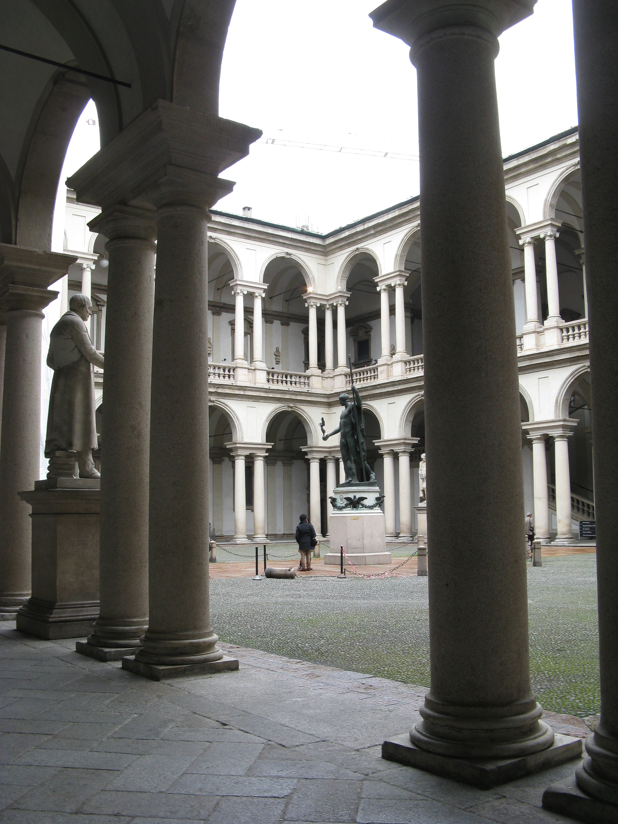 Stone columns frame the arcaded courtyard and central bronze statue at Palazzo di Brera in Milan.