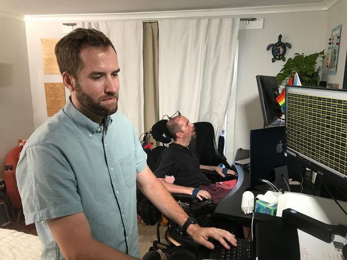 Nicholas Card getting the BCI system ready, with Casey Harrell behind him.